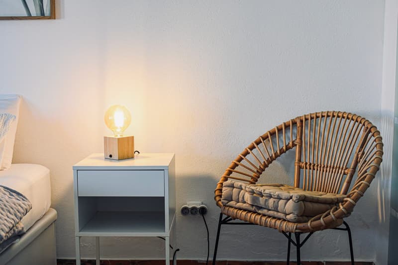 Warm bedside lamp next to a rattan chair in the evening light